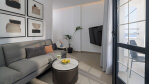 A modern living room with a grey sofa, a round coffee table with a bowl of fruit, a potted plant, and artwork on the wall. - Angel Apartments 2 (Koutouloufari)