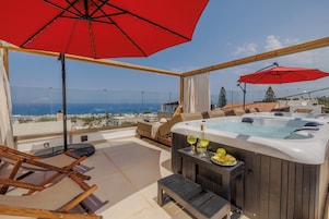 A rooftop terrace with a hot tub, lounge chairs, and a red umbrella.