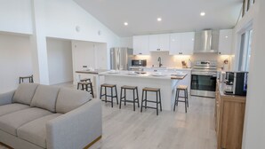 A modern kitchen with white cabinets, a central island with stools, a built-in oven, and a coffee machine. - 6BR Waterfront Escape | Perfect for Multi-Family Groups (Harcourt)