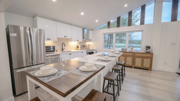 A modern kitchen with white cabinetry, stainless steel appliances, and a long island with bar stools. - 6BR Waterfront Escape | Perfect for Multi-Family Groups (Harcourt)