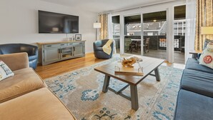 En moderne stue med sofa, sofabord og TV. Der er en skydedør, der fører ud til en balkon.