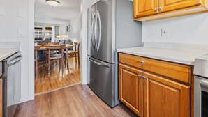 Una cocina moderna con armarios de madera, un refrigerador de acero inoxidable y un comedor con una mesa y sillas de madera.