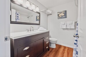 A bathroom with a dark wooden vanity, a white sink, and a toilet. There are towels hanging on a rack and a framed picture on the wall. - Nye Beach, Restaurants, Shop! Walk to the Beach! (Newport)