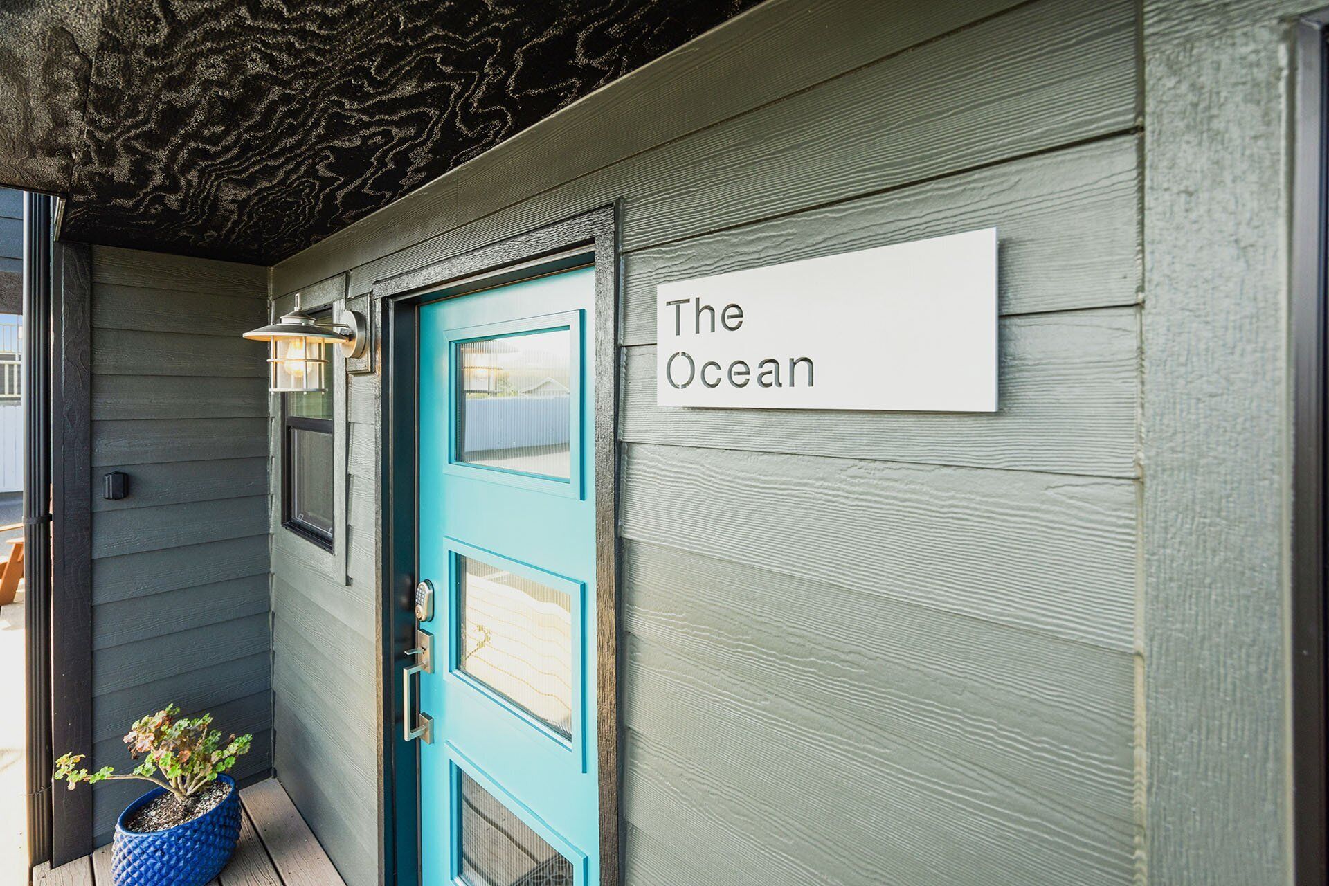 En turkis dør med et skilt, hvor der står "The Ocean", på en træfacade.