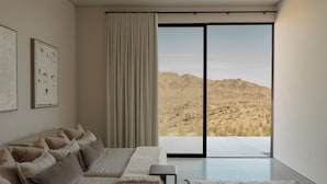 A modern bedroom with a large window offering a view of a desert landscape.