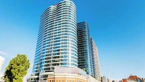 Un immeuble moderne de grande hauteur, doté d’une façade incurvée, de nombreux balcons et, en arrière-plan, d’un ciel bleu azur.