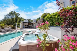 A swimming pool with a hot tub, lounge chairs, and a modern house in the background.