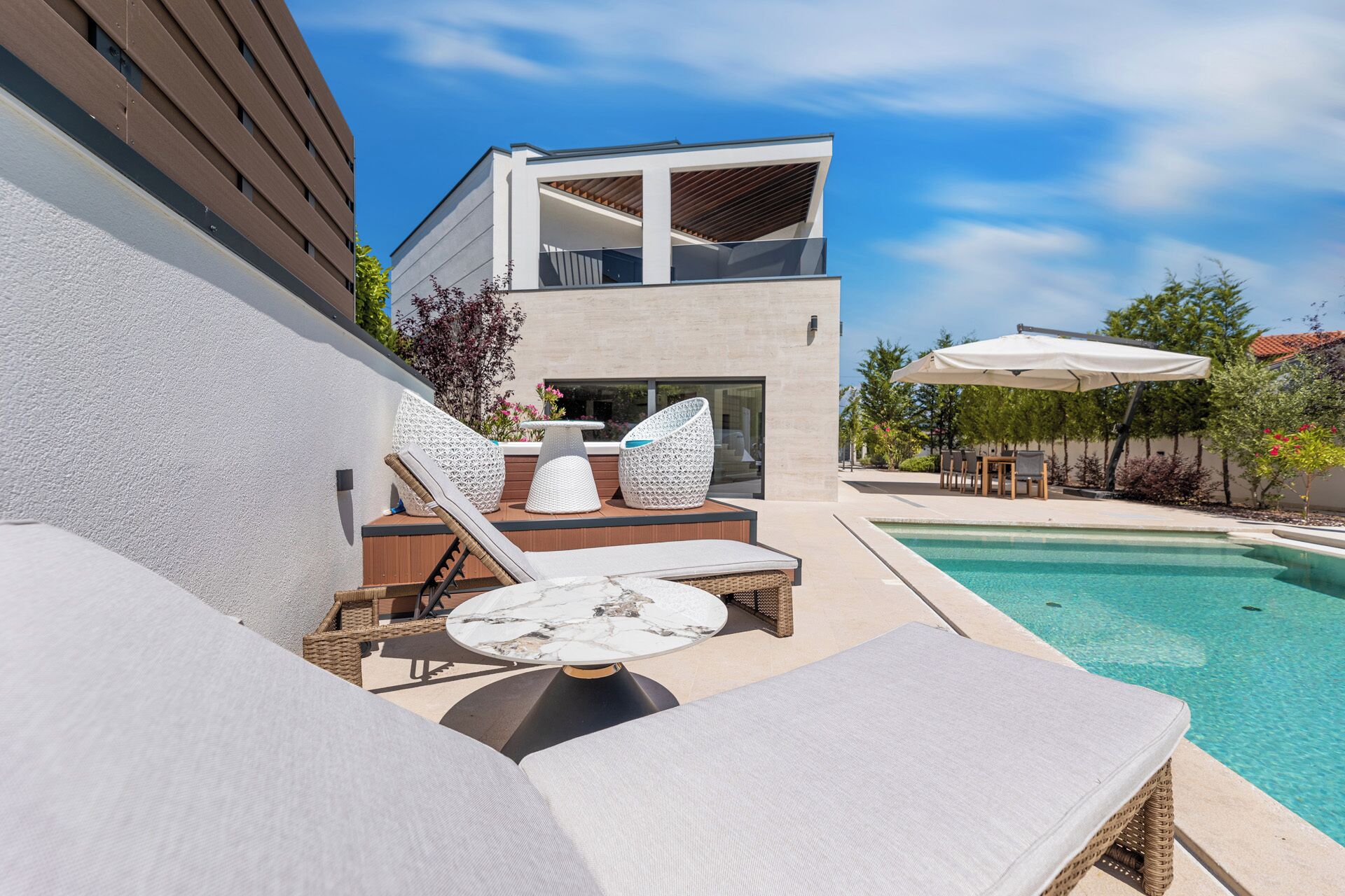 A modern outdoor pool area with lounge chairs and a table, surrounded by a building with a balcony.