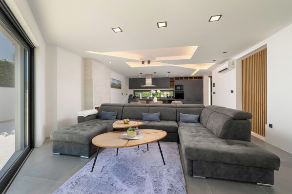 A modern living room with a sectional sofa, a coffee table, and a view of the kitchen.