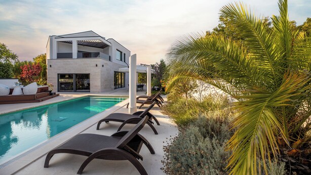 A modern house with a swimming pool, lounge chairs, and a palm tree.
