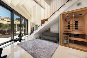 A modern interior with a staircase, a grey sofa, a wooden wine rack, and a large window overlooking an outdoor area.