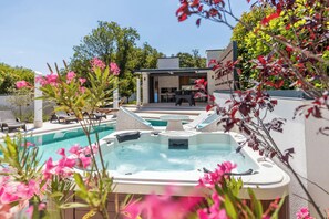 A pool area with hot tubs, lounge chairs, and a building in the background.