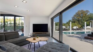A modern living room with a large flat-screen TV, grey sofas, and a small round table.