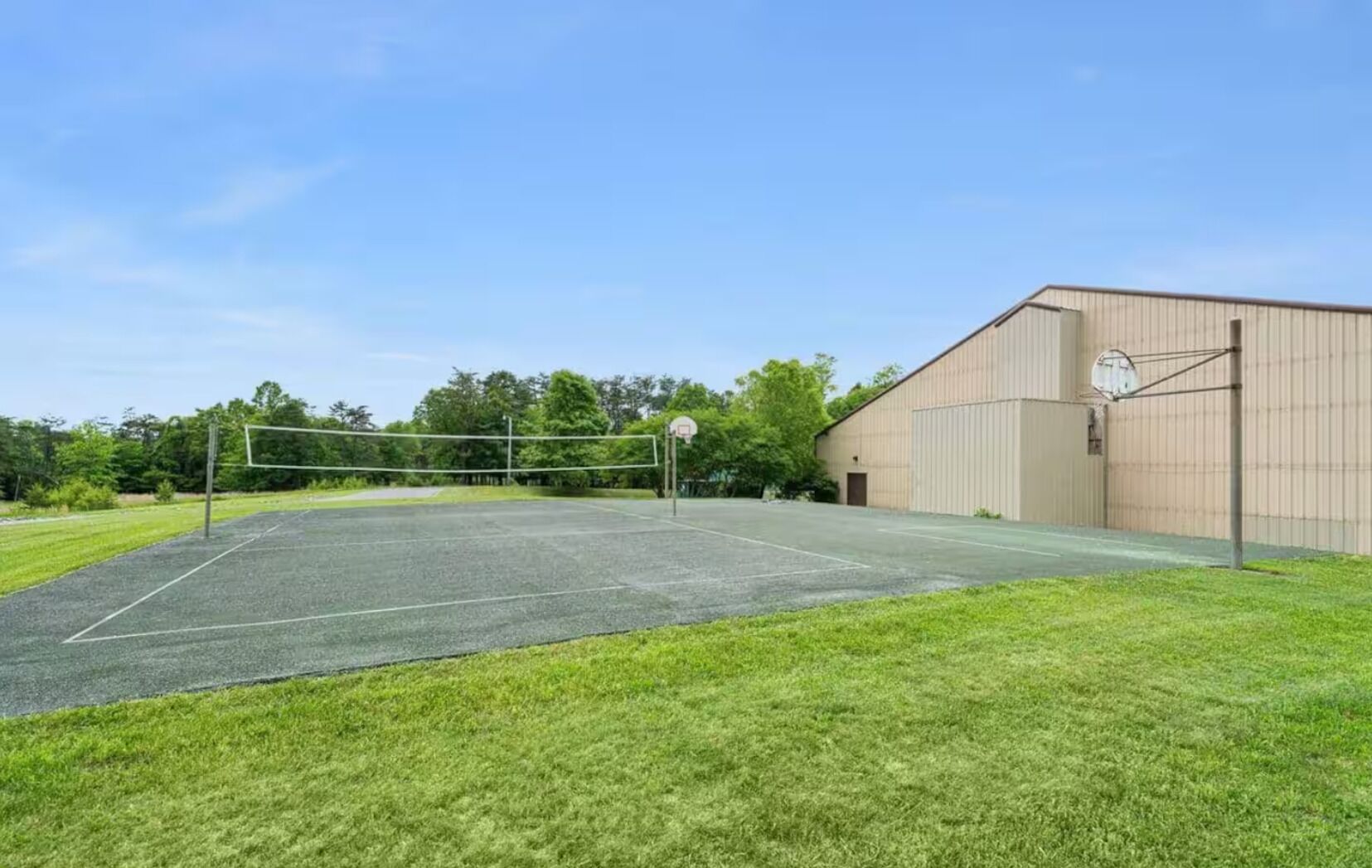 Un court de tennis en plein air, doté d’un filet, entouré d’une pelouse et avec un grand bâtiment en arrière-plan.