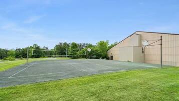Un court de tennis en plein air, doté d’un filet, entouré d’une pelouse et avec un grand bâtiment en arrière-plan.