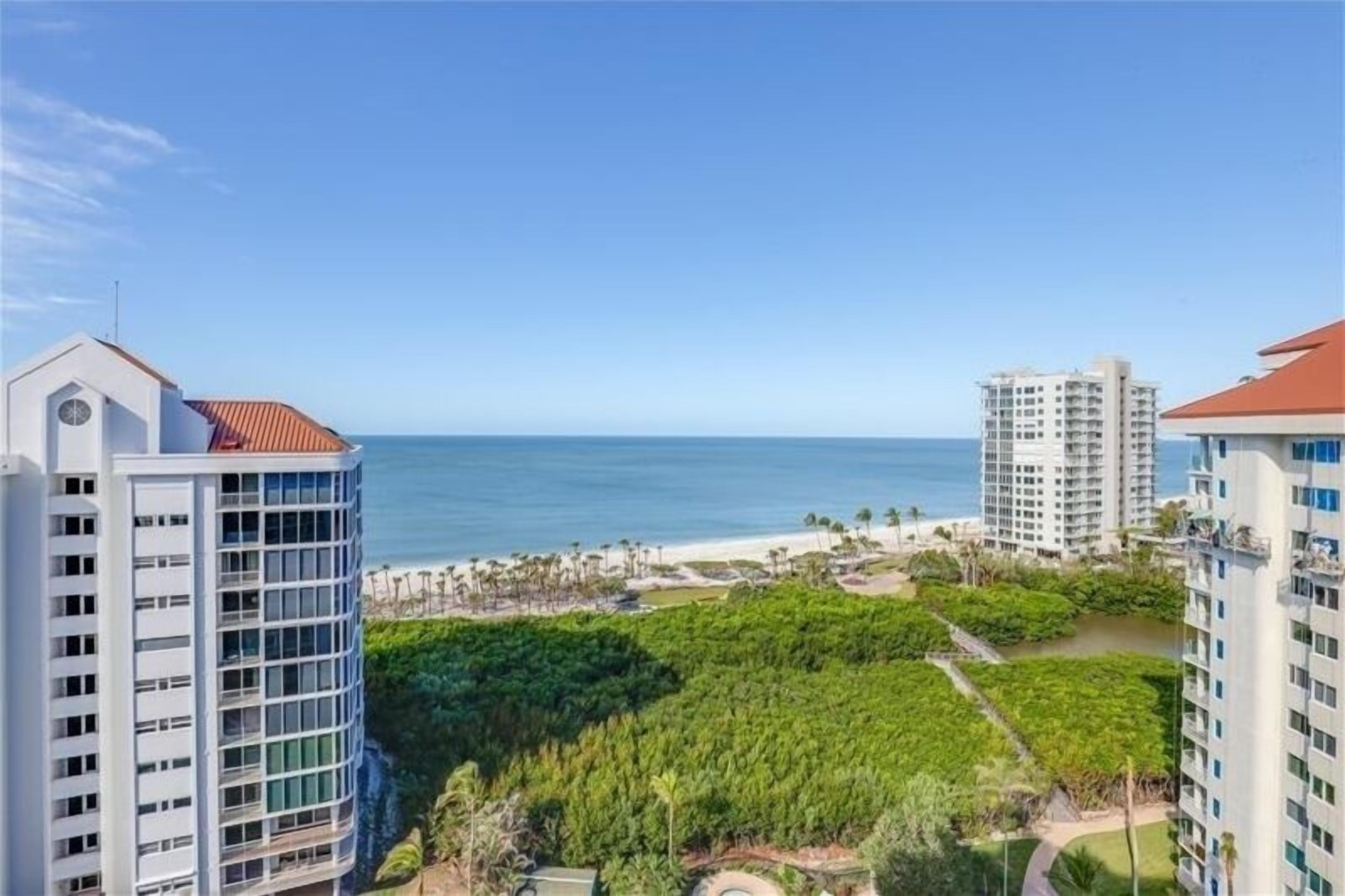 A high-rise building with a view of the ocean and a landscaped area with trees and pathways.