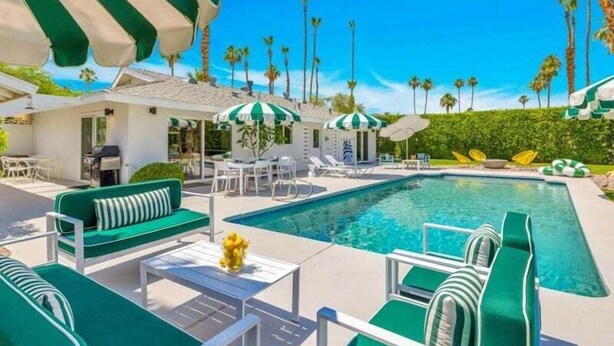 A pool area with green and white striped umbrellas, lounge chairs, and a clear blue sky.