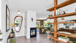 A modern living room with a fireplace, wooden shelves, and a view of the outdoors.