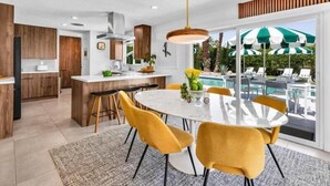 A modern kitchen with wooden cabinets, a central island, and a dining area with yellow chairs.