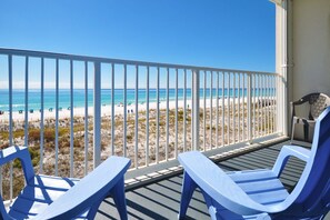 A balcony with two blue chairs overlooking a beach.