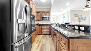 A kitchen with stainless steel appliances, wooden cabinets, a marble countertop, and a view of the outdoors.