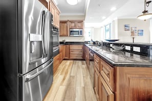 Une cuisine dotée d’appareils électroménagers en acier inoxydable, de meubles en bois, d’un plan de travail en marbre et offrant une vue sur l’extérieur.