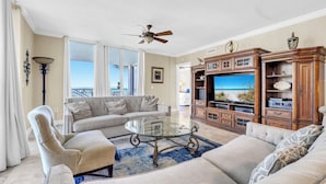 A living room with a glass coffee table, beige sofas, a television, and a wooden entertainment unit.