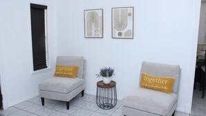 Ein Zimmer mit zwei Sesseln, einem kleinen runden Tisch mit einer Pflanze und zwei gerahmten abstrakten Kunstwerken an der Wand.