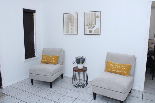 A room with two armchairs, a small table with a plant, and two framed abstract artworks on the wall.