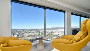 Une chambre moderne avec de grandes fenêtres, deux fauteuils jaunes et une petite table sur laquelle se trouvent une bouteille et des verres.