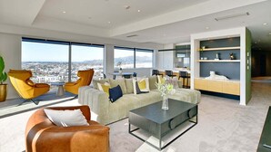 Un salon moderne avec un canapé, des fauteuils et une table basse. Une grande fenêtre offre une vue sur la ville.