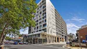 A modern multi-story hotel with a unique facade design, located at a street corner with visible cars and pedestrians.