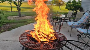 A metal fire pit with flames, surrounded by outdoor furniture and a house in the background. - Perfect 1-bedroom apartment in Marlette unit 2 (Marlette)