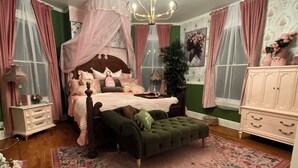 Ett sovrum med en himmelssäng, en grön, tuftad soffa, en rosa matta med blommönster och en vit byrå.