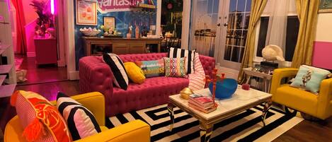Un salon lumineux, avec un canapé rose, un fauteuil jaune et un tapis à rayures.