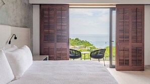A bedroom with a large bed, a nightstand, a lamp, and a view of the ocean through open wooden shutters. - Iyari Estates Punta Mita Villa with Ocean Views and Pool (Corral del Risco)