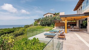 A modern outdoor living area with a glass balustrade, lounge chairs, and a pool. - Iyari Estates Punta Mita Villa with Ocean Views and Pool (Corral del Risco)