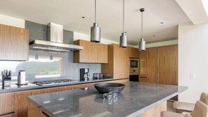 A modern kitchen with a large island, wooden cabinets, stainless steel appliances, and pendant lighting. - Iyari Estates Punta Mita Villa with Ocean Views and Pool (Corral del Risco)