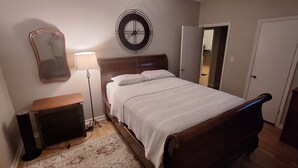 A bedroom with a bed, a bedside table, a lamp, a mirror, a clock, and a television.
