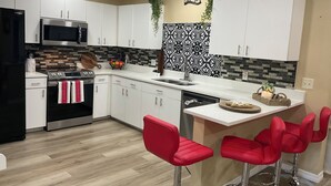 Una cocina moderna con armarios blancos, electrodomésticos de acero inoxidable, salpicadero blanco y negro y taburetes rojos.