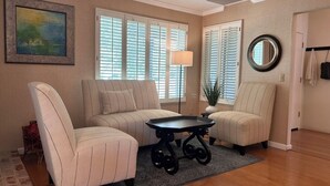 A living room with two beige armchairs, a black coffee table, and a large window with blinds. - Ham Station - 3 B / 2 BA - Bright & Cheery Home - A Dog’s Dream! (LODI)