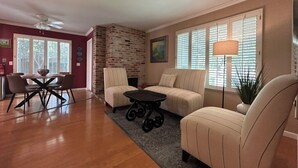 A living room with a sofa, a dining table with chairs, a small table, and a brick wall. - Ham Station - 3 B / 2 BA - Bright & Cheery Home - A Dog’s Dream! (LODI)