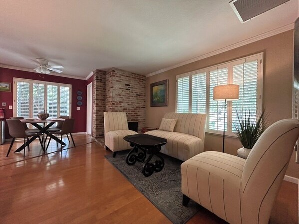A living room with a sofa, a dining table with chairs, a small table, and a brick wall.