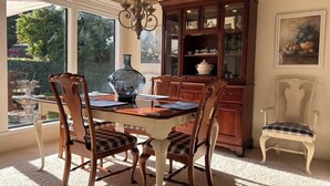 A dining area with a wooden table and chairs, a chandelier, a cabinet with glass doors, and a window with a view of greenery. - Ham Station - 3 B / 2 BA - Bright & Cheery Home - A Dog’s Dream! (LODI)