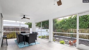 Een wintertuin met een eethoek, grote ramen en een plafondventilator.