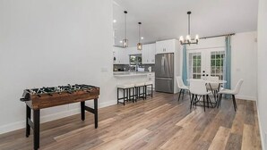 Een moderne keuken met een tafelvoetbaltafel, barstoelen en een eethoek met witte stoelen en een tafel.