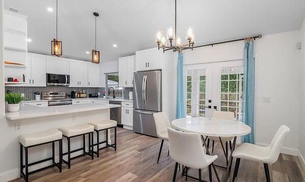 A modern kitchen with white cabinetry, stainless steel appliances, and a central island with bar stools.