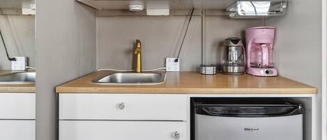 Een compacte keuken met een houten aanrecht, een roestvrijstalen spoelbak, een gouden kraan, een roze koffiezetapparaat, een zilveren waterkoker en een inbouwvaatwasser.