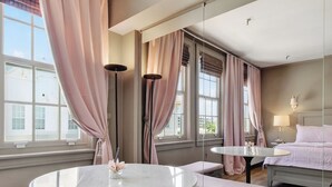 Une pièce avec une table ronde, des bancs, un lit et de grandes fenêtres avec des rideaux.