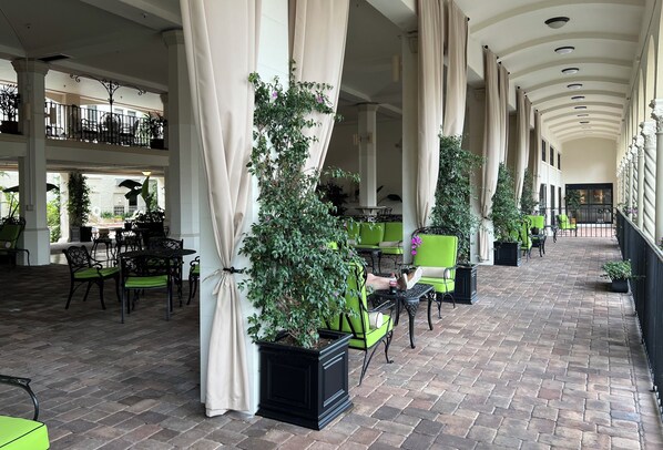 A covered outdoor area with brick flooring, green and black chairs, and potted plants.